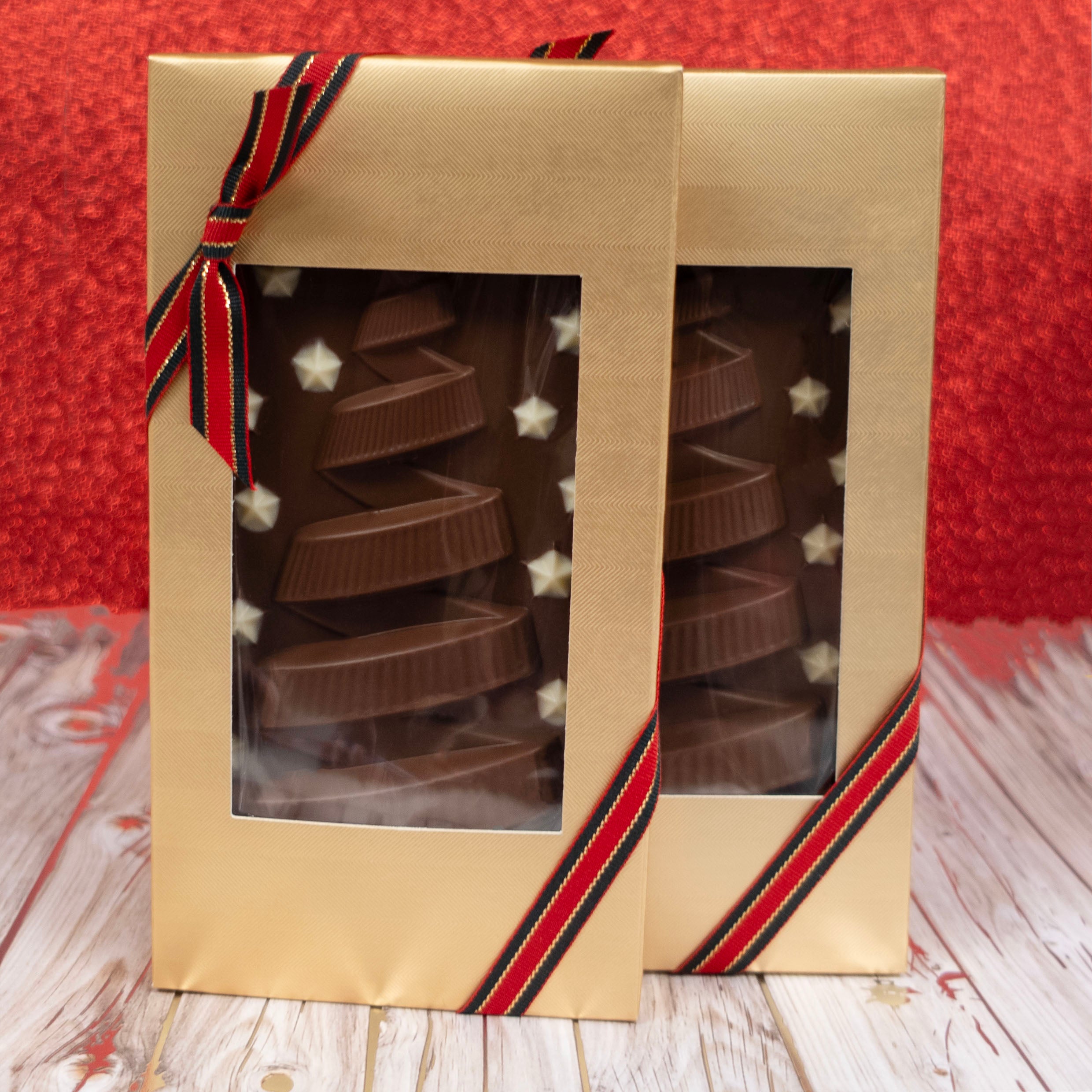 Two christmas chocolate bars in a decorative box with a red ribbon on a wooden surface.