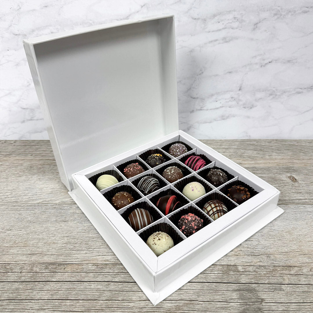 Open white box filled with assorted chocolates on a wooden surface.