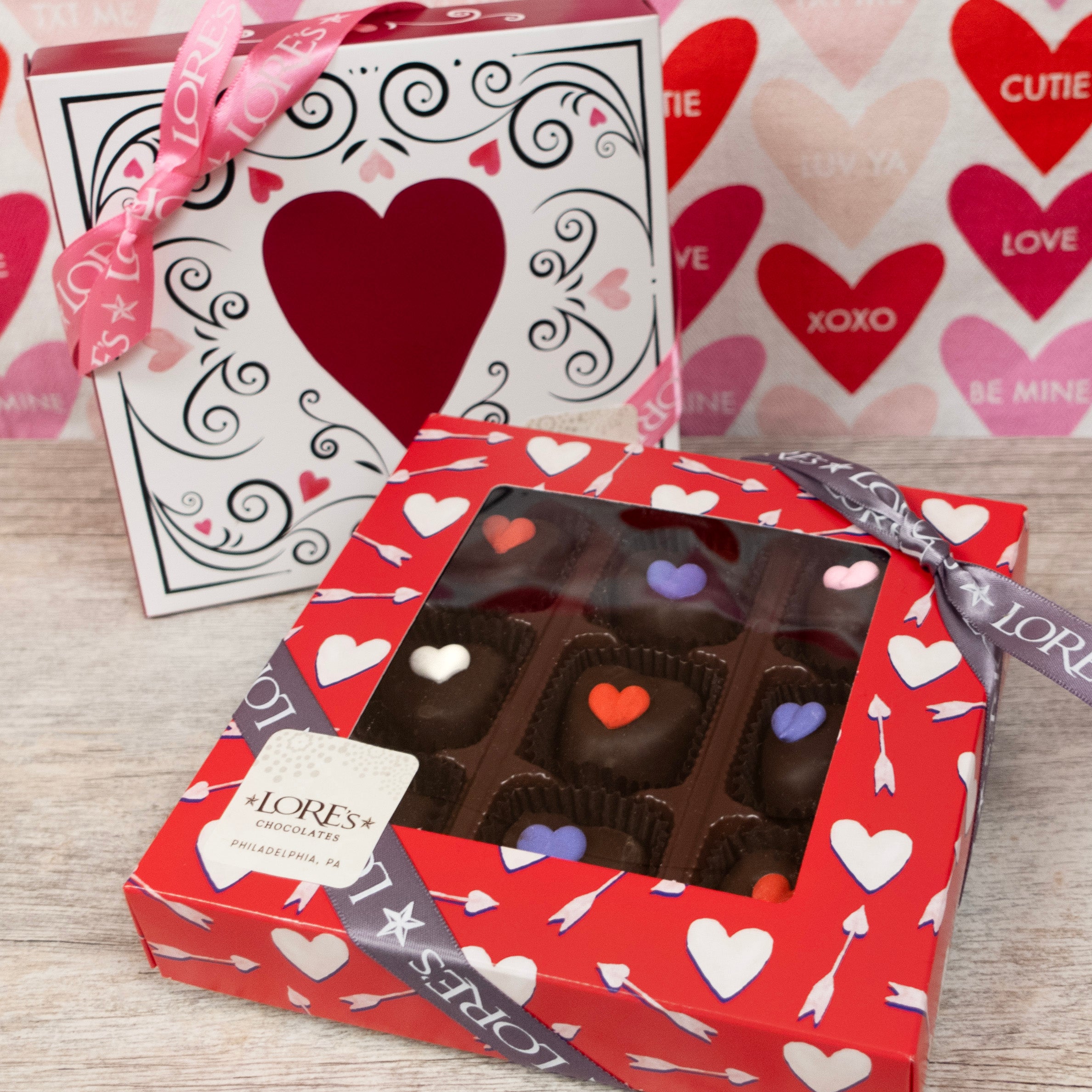 Red window bow with white hearts and arrows, showing the contents of Lore's decorated dark chocolate hearts filled with mint cream. Other box design in background.