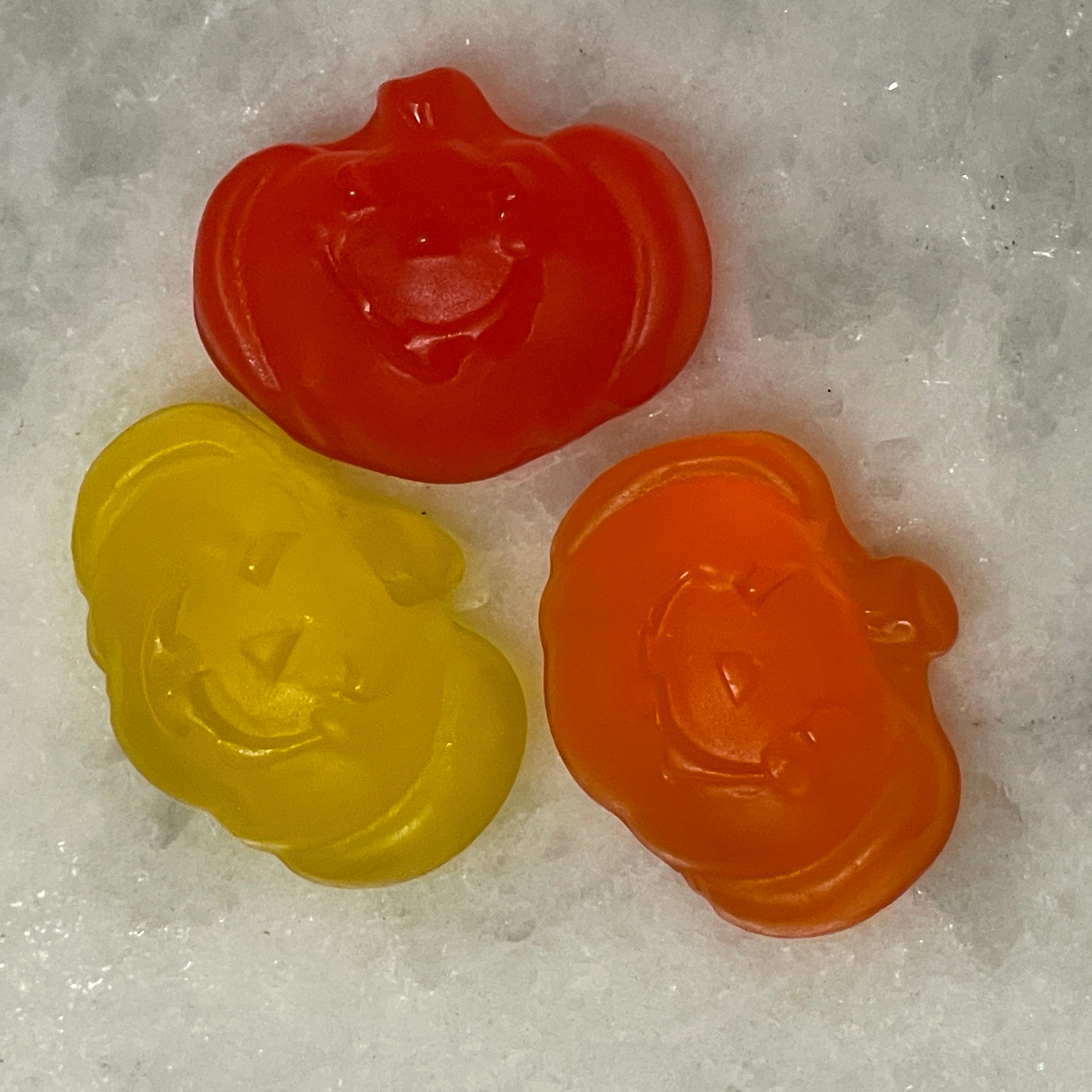 Orange, red, and yellow gummy pumpkins with smiling jack-o-lantern faces.