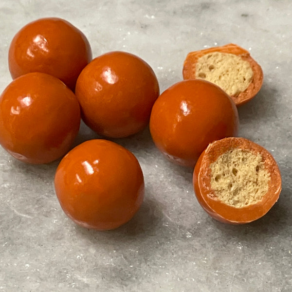 Orange pumpkin pie flavored malt balls. One is cut open to show malted inside.