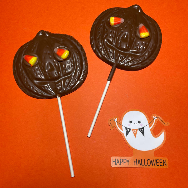 Two milk chocolate lollipops shaped like jack-o-lantern pumpkins with candy corn eyes.