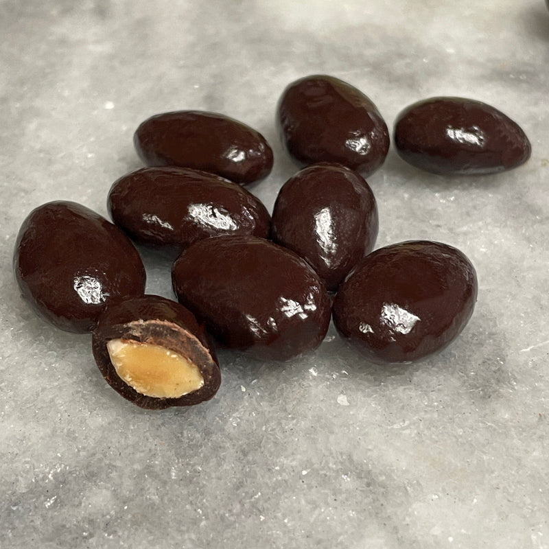 Almonds covered in a tasty dark chocolate, image shows a pile with one halved to see the almond inside