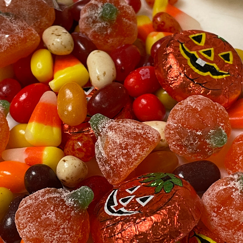 Close up of treat-or-treat favor candies: milk chocolate foiled pumpkins, autumn jelly beans, candy corn, and sour gummy pumpkins