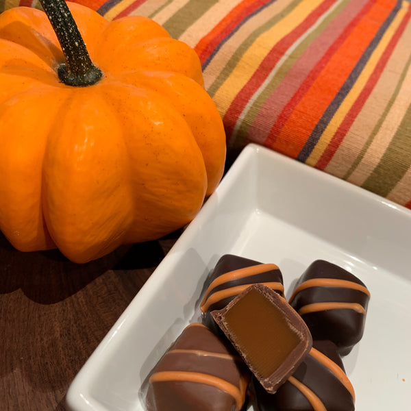 Fresh pumpkin spice caramels covered in dark or milk chocolate with a decorative orange drizzle - one cut in center to show the amazing soft chew caramel